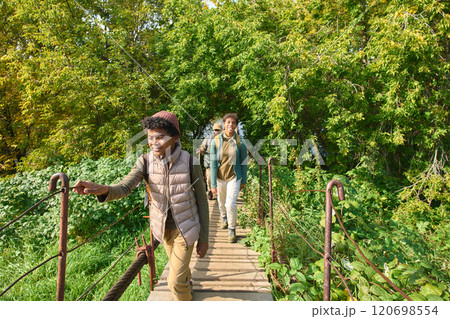 Curious African American boy going on wooden old bridge while his parent and older sister following him in background 120698554