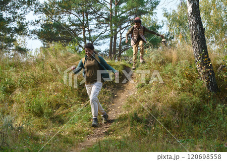 Sister and young brother wearing hiking outfit running from hill in forest during active vacation 120698558