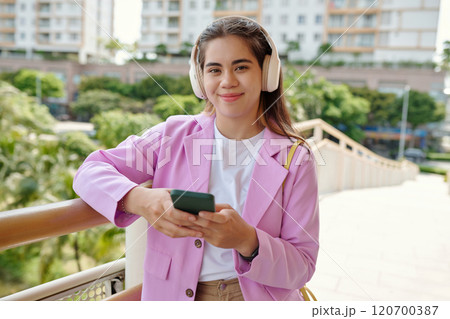 Smiling Young Woman Listening Music with Headphones Outdoors 120700387