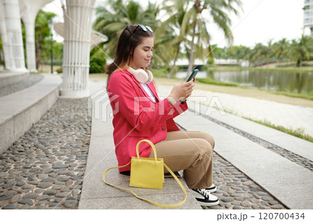 Young Woman Sitting Outside Checking Her Smartphone Young Woman Sitting Outside Checking Her Smartphone 120700434