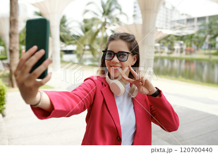Smiling Woman Taking Selfie Outdoors with Peace Sign 120700440