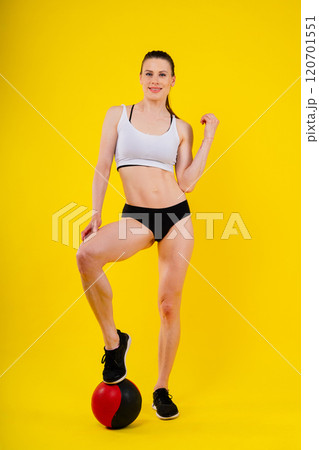 Sportive caucasian cross fit woman with fitness ball, look at camera. Studio dark yellow background 120701551