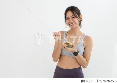 Asian attractive lady sportswear healthy eating salad vegetables over white background. Female holding salad bowl various vegetables and fruit healthy food for weight loss and exercise. Asian attractive lady sportswear healthy eating salad vegetables over white background. Female holding salad bowl various vegetables and fruit healthy food for weight loss and exercise. 120702025