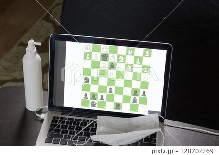 Chess task on laptop screen online. Near antibacterial spray and medical mask. Leisure in self-isolation. International chess day. 120702269