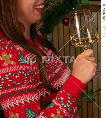 shot of young woman smiling while holding a glass with white wine or champagne wearing a red Christmas sweater 120704316
