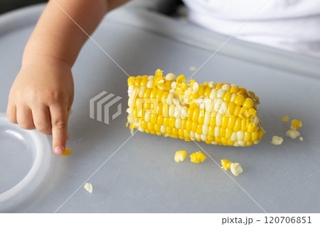 Baby picking sweet corn kernels from the table. Closeup. 120706851