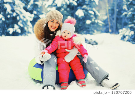 Winter happy smiling mother and child sitting on sled in snowy day 120707200