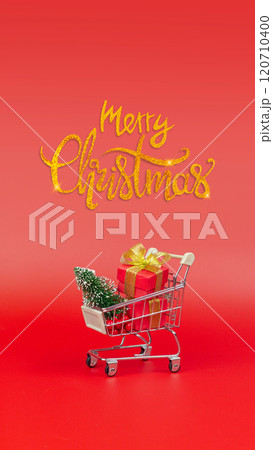 Merry Christmas inscription and a trolley with gifts and a Christmas tree. Buying gifts, preparing for the holidays vertical minimal banner 120710400