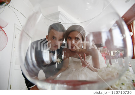 The bride and groom look at the camera through a glass. 120710720