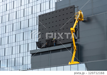 Two workers in hard hats mount elements of outdoor video advertising 120712168
