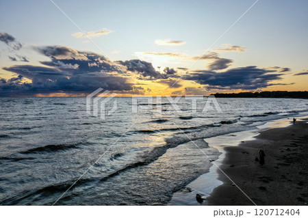 Tranquil sunset over the serene beach with gentle waves and dramatic clouds in the evening sky Tranquil sunset over the serene beach with gentle waves and dramatic clouds in the evening sky 120712404