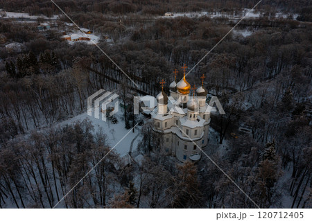 Snow-covered church nestled in a tranquil forest during winter sunset near a peaceful village 120712405