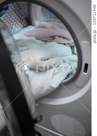 View of the tumble dryer or washing machine with the door open and a towel inside 120712448