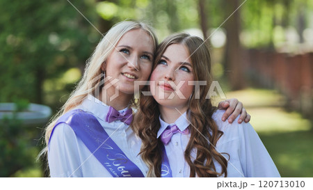 Two happy graduates in a park. Wearing purple ribbons. Embracing on their last day of school. Filled with hope and dreams for the future 120713010