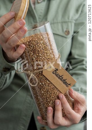 Woman holding Raw buckwheat porridge in sustainable natural packaging. Refillable glass jar. Gluten free cereals. Health gut benefits. Concept of alternative whole spelt grain ingredient. Vegetarian Woman holding Raw buckwheat porridge in sustainable natural packaging. Refillable glass jar. Gluten free cereals. Health gut benefits. Concept of alternative whole spelt grain ingredient. Vegetarian 120713625