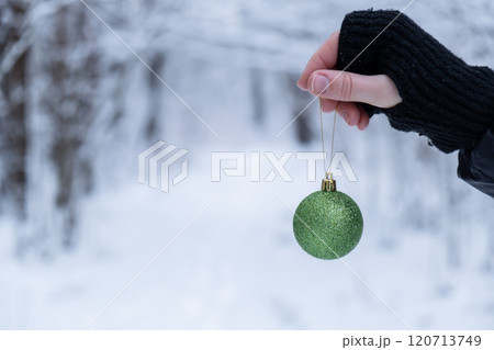 Female hands holding Christmas decoration outdoor in snowy winter forest. Postcard greeting card mock up. Holiday green ball toy branch Ornaments Female hands holding Christmas decoration outdoor in snowy winter forest. Postcard greeting card mock up. Holiday green ball toy branch Ornaments 120713749