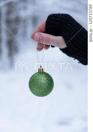 Unrecognizable woman hangs Christmas decoration outdoor in snowy winter forest. Postcard greeting card mock up. Holiday green ball toy branch Ornaments 120713789