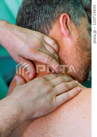 Therapeutic practitioner applies gentle pressure on neck, shoulders of client, aiming to relieve tension promote relaxation in massage parlor calm indoor environment. 120714835