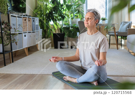 Happy smiling mature middle-aged woman with gray hair does exercises at home and does yoga. 120715568