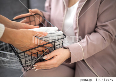 Female hands putting neatly folded clothes linen domestic textile metallic basket closeup top view 120715575