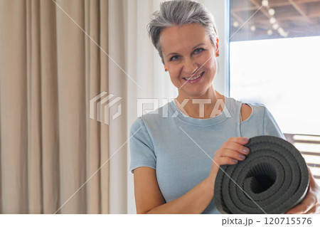An elderly smiling yogi woman with gray hair is going to practice at home. A mature woman 120715576