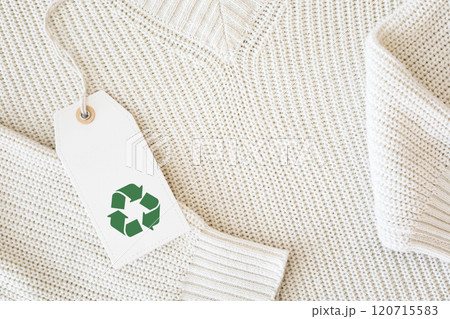 White knitted clothing with a white label featuring the recycling symbol. 120715583