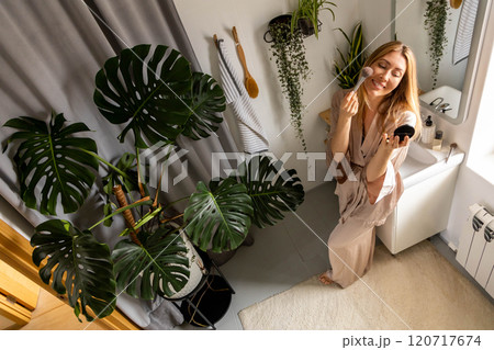A well-groomed and beautiful woman combs her hair in front of a mirror in her bathroom. 120717674