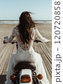 浜辺でバイクに乗っているウェディングドレス姿の女性 120720858