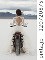 砂漠でバイクに乗っているウェディングドレス姿の女性 120720875