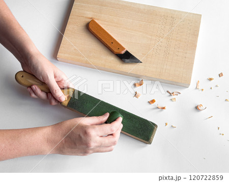 Hands sharpening tool with strop next to cutting board and carving knife 120722859