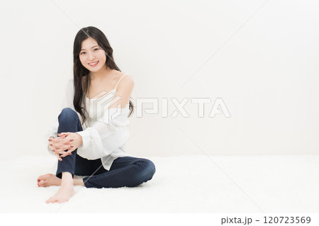 スキニージーンズ・ジーパン・デニムパンツをはいて胡座をかいて座る若い女性 120723569