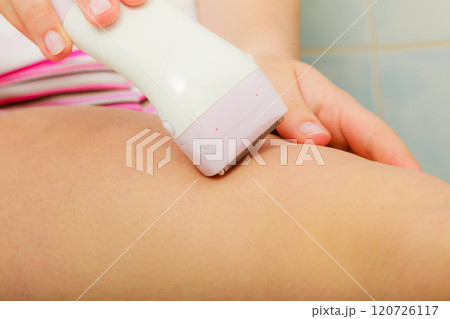 Woman shaving legs with depilator in bathroom Woman shaving legs with depilator in bathroom 120726117