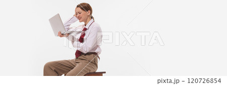 Banner. Professional young woman in white shirt and red tie sits on stool, visibly stressed while holding laptop against white studio background. 120726854