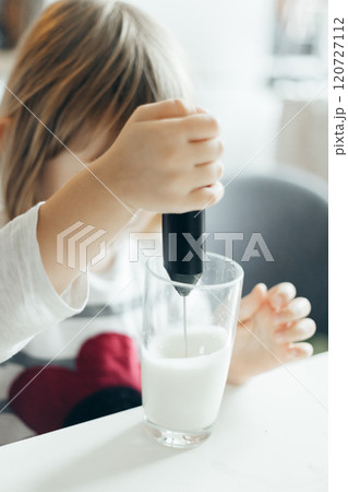 Pre-school child makes frothy milk with a hand mixer in a glass cup in the kitchen Pre-school child makes frothy milk with a hand mixer in a glass cup in the kitchen 120727112