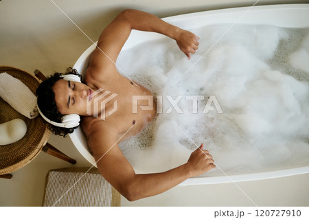 Top down shot of mixed race man lying in hot bath listening to music while takin nap 120727910