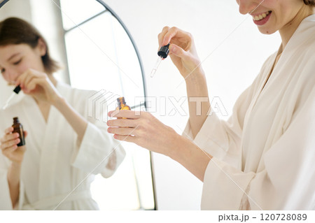 Medium close up of unrecognizable woman holding glass bottle with serum while using it for hand skin 120728089