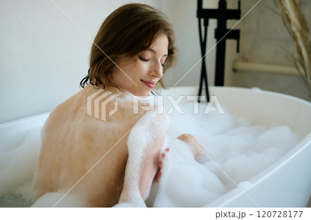 Back view shot of attractive Caucasian woman washing her body with delicate foam while taking bath at home Back view shot of attractive Caucasian woman washing her body with delicate foam while taking bath at home 120728177