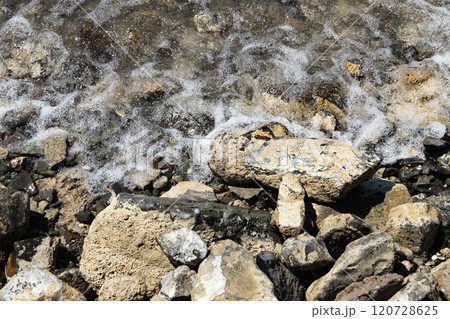 Waves gently wash over a rocky shore under the warm sun at a secluded beach location Waves gently wash over a rocky shore under the warm sun at a secluded beach location 120728625