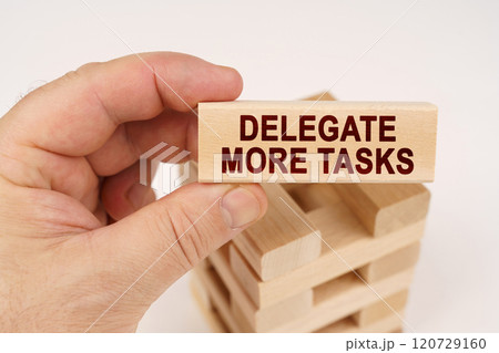 A man holds in his hands a wooden block with the inscription - Delegate More Tasks A man holds in his hands a wooden block with the inscription - Delegate More Tasks 120729160
