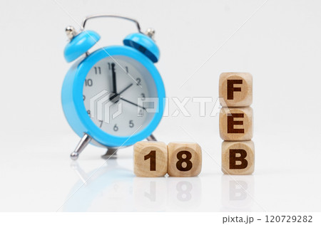 On a white background, a blue alarm clock and a calendar with the inscription - February 18 On a white background, a blue alarm clock and a calendar with the inscription - February 18 120729282