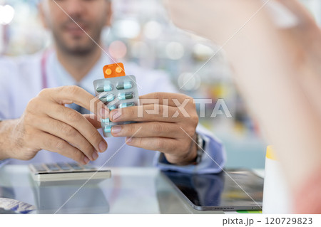 Man pharmacist holding medicine capsule blister pack at counter dispensing medicine in pharmacy drugstore. Dispensing medication to patients. Man pharmacist holding medicine capsule blister pack at counter dispensing medicine in pharmacy drugstore. Dispensing medication to patients. 120729823
