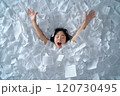 A young woman overwhelmed by paperwork, expressing frustration in a sea of documents at home 120730495