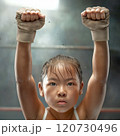 Young girl training in a boxing gym, focused and determined, with gloves raised in the air 120730496