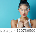 Confident young woman posing against a blue background showcasing strength and determination 120730500