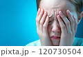 A young child covers their face with their hands, showing distress against a blue background 120730504