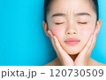 Young woman with a distressed expression holds her face against a bright blue background 120730509