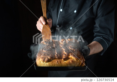 A baker holds a steaming tray of freshly baked bread, its golden crust glistening under the soft glow of kitchen lights. The aroma fills the air, inviting all to savor its warmth 120730514