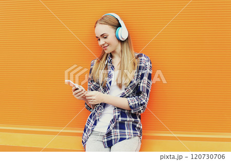 Smiling girl in headphones listens to music and using smartphone over orange background 120730706