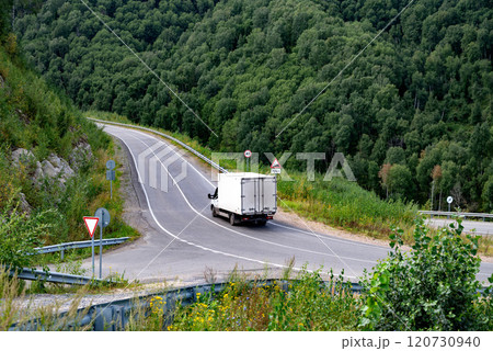 Cargo truck driving on a winding road surrounded by lush green forest. 120730940