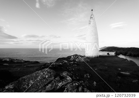 A white lighthouse rises prominently on the rocky coastline, surrounded by grass and cliffs. The calm ocean stretches out under a clear blue sky, evoking a sense of tranquility. A white lighthouse rises prominently on the rocky coastline, surrounded by grass and cliffs. The calm ocean stretches out under a clear blue sky, evoking a sense of tranquility. 120732039
